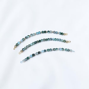 May include: Three curved strands of beads featuring a mix of blue, green, and teal mottled stones interspersed with small metallic gold and silver spacer beads. Each strand is finished with a small wire loop at both ends for attachment.