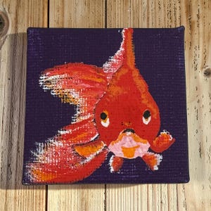 May include: A square canvas painting of a goldfish. The fish is painted in shades of orange, red, and white, with a purple background. The goldfish has large eyes and a detailed fin.