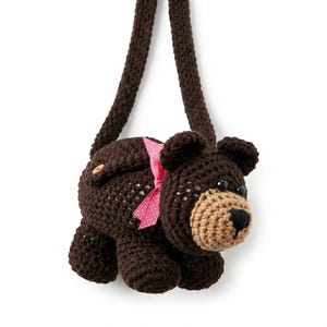 May include: A brown crochet bear-shaped purse with a long strap. The bear has a tan muzzle, black nose, and small black eyes. A pink ribbon with white polka dots is tied around the bear's neck. The purse has a wooden button closure.