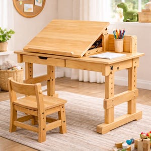 May include: A light-coloured wooden desk with an adjustable tilting tabletop and a matching wooden chair. The desk features a flat surface area, a pencil holder with coloured pencils, and a drawer. The legs of the desk and chair are adjustable.