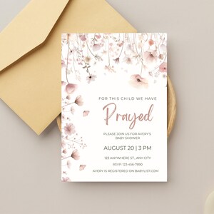 Può includere: Un invito per un baby shower con accenti floreali e il testo "For this child we have Prayed". L'invito è bianco con illustrazioni floreali rosa e pesca. Una busta è sullo sfondo.