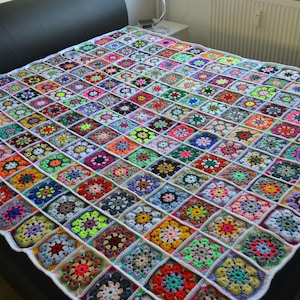 Könnte beinhalten: Eine handgefertigte, farbenfrohe Häkeldecke mit Patchwork-Design. Die Decke zeigt eine Vielzahl von bunten Quadraten in Rot-, Blau-, Grün-, Gelb- und Lilatönen, die in einem Rastermuster angeordnet sind. Die Decke liegt auf einem Bett.