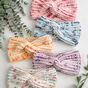 Puede incluir: Colección de seis diademas de ganchillo hechas a mano en varios colores. Las diademas presentan un diseño de nudo retorcido y son en tonos de rosa, azul, naranja, morado y crema con motas coloridas. Se muestran sobre una superficie blanca.