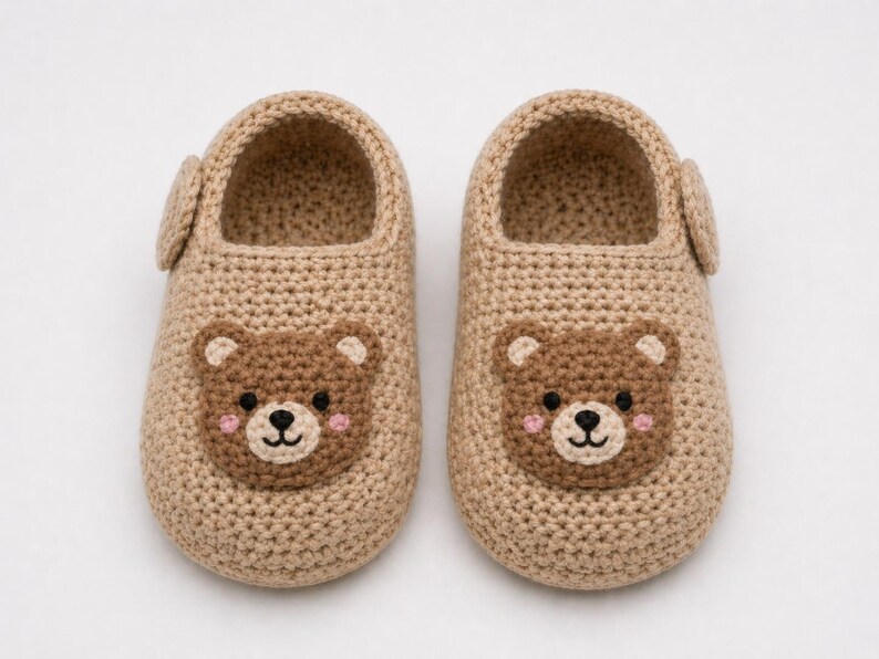 Puede incluir: Un par de zapatillas de beb&eacute; de ganchillo beige. Cada zapatilla presenta una cara de oso marr&oacute;n con mejillas rosas, una nariz y ojos negros. Las zapatillas tienen una peque&ntilde;a correa lateral y est&aacute;n dise&ntilde;adas para la comodidad y el calor.