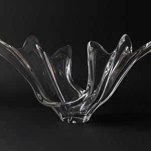 Puede incluir: Un cuenco decorativo de vidrio transparente con un diseño único y fluido. El cuenco tiene una forma amplia y abierta con múltiples bordes curvos, que se asemejan a pétalos u olas. El vidrio es transparente.
