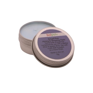 May include: A silver tin of "Smurf Poo" honing and stropping paste, with the lid open. The label is purple and white, detailing the product's use for tool and knife sharpening. The paste inside is light blue. Made in the UK, 15g.
