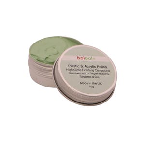 May include: An open metal tin with a light green polish, next to its lid. The lid has text that reads "Plastic & Acrylic Polish", a high gloss finishing compound that removes imperfections and restores shine. The label also states "Made in the UK" and the weight is 15g.