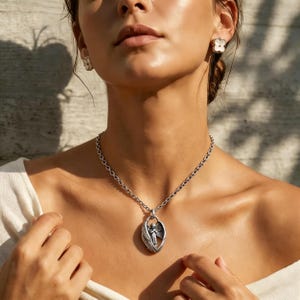 May include: A silver necklace with a pendant depicting an angel within a wing design. The chain is a link style, and the necklace is worn with matching flower earrings. The jewellery is shown against a neutral background.