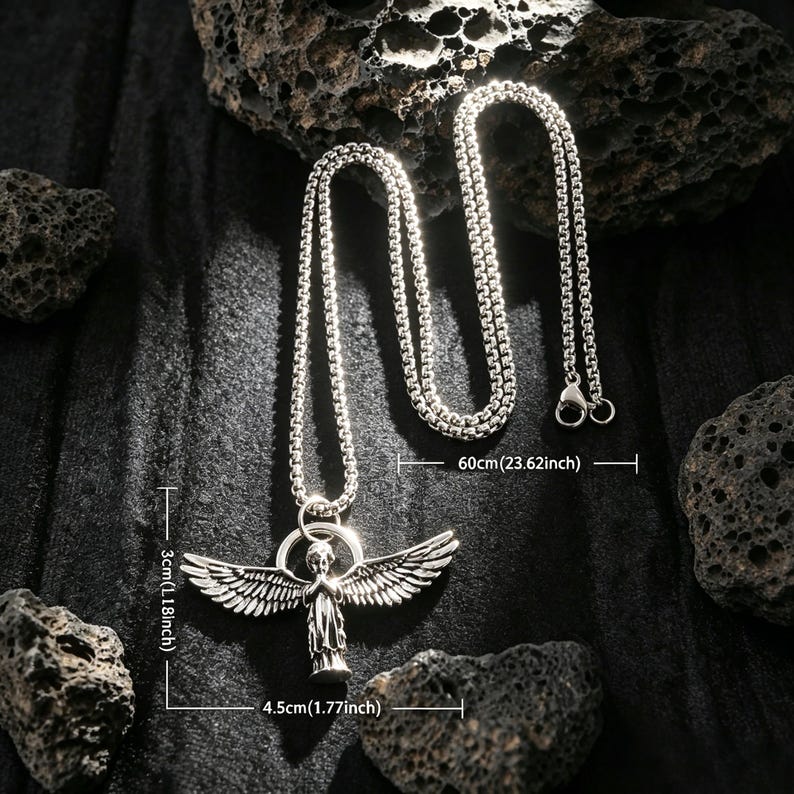 May include: Silver necklace with an angel pendant. The pendant is 4.5 cm wide and 3 cm tall. The chain is 60 cm long. The necklace is shown against a dark backdrop with rough, dark grey rocks, highlighting the jewellery's design.