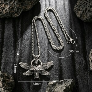 May include: Silver necklace with a pendant depicting a winged figure. The pendant is 48mm wide and 38mm high. The chain is 60cm long. The necklace is shown on a dark, textured background.