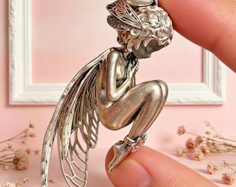 Colgante de ángel de inspiración Art Nouveau con acabado en plata oxidada: figura detallada en cuclillas con alas superpuestas y detalle en el tobillo.