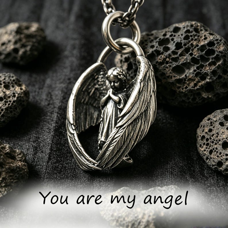 May include: A silver pendant necklace with an angel figure enclosed by wings. The angel is depicted with hands clasped in prayer. The words "You are my angel" are at the bottom. The necklace hangs on a chain.