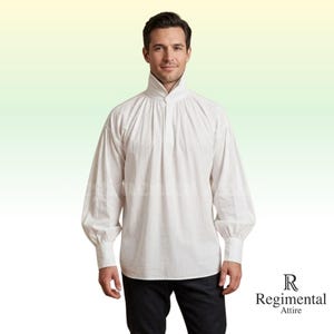 Puede incluir: Una camisa blanca de manga larga con cuello alto y detalles fruncidos. La camisa tiene un corte holgado con mangas amplias que se recogen en las muñecas. El logotipo de Regimental Attire es visible.