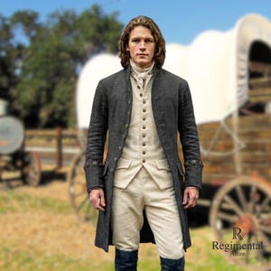 May include: A charcoal gray long coat with gold buttons, worn over a cream-colored vest and pants. The outfit is completed with a white cravat and dark blue boots. The image features a man in historical attire, with a blurred background of a wagon.