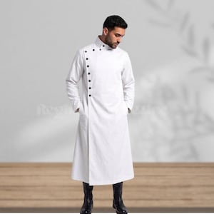 May include: A white long coat with a high collar and black buttons down the front. The coat has long sleeves and pockets. The person in the image is wearing black boots. The coat is a unique style of outerwear.