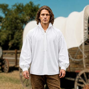 May include: A long-sleeved white shirt featuring a high collar with a lace-up front closure, loose-fitting sleeves with buttoned cuffs, and a relaxed silhouette. The shirt is made of a solid white fabric and has a classic, historical-inspired design.