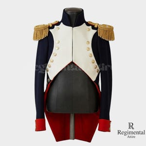 Può includere: Giacca militare blu navy con gilet bianco, bottoni dorati e spalline dorate. La giacca ha polsini rossi e coda rossa. La giacca è esposta su un manichino nero.