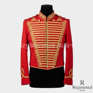 May include: A red military-style jacket with gold-colored trim and buttons. The jacket features a high collar and decorative gold braid. The sleeves are long, and the jacket is displayed on a black mannequin. The jacket is a formal garment.