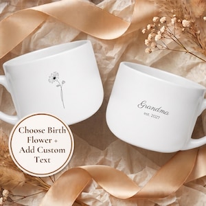 May include: Two white ceramic mugs with handles. One mug features a black line drawing of a single daisy flower. The other mug displays the black text "Grandma" above "est. 2027". A circular label reads "Choose Birth Flower + Add Custom Text".