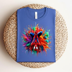 May include: Blue t-shirt featuring a colorful graphic of Spider-Man hanging upside down. The design includes vibrant paint splatters in red, orange, green, and purple. The shirt is made of a soft material and is suitable for casual wear.