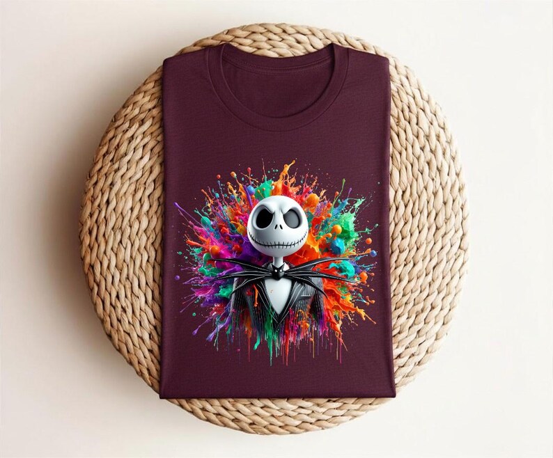 May include: A dark maroon t-shirt featuring a graphic print of a white skeletal character with a stitched mouth, wearing a black pinstripe suit and bow tie, centered against a vibrant, multi-colored paint splatter background with bright hues.