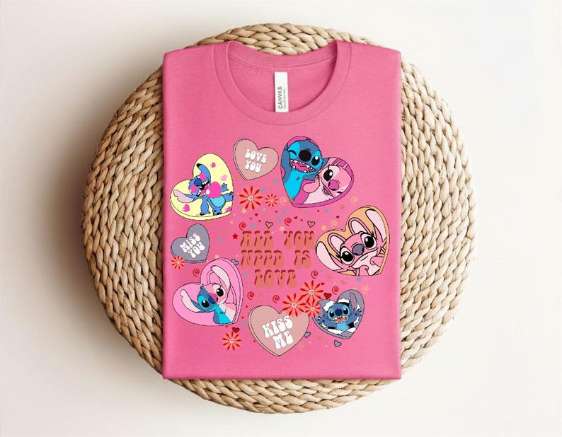 Peut inclure: Un t-shirt rose avec des personnages de dessins anim&eacute;s et des motifs en forme de c&oelig;ur. Le t-shirt porte l'inscription "ARE YOU HAPPY IS LOVE" et "LOVE YOU", "MISS YOU" et "KISS ME" sur les c&oelig;urs. Le t-shirt est pli&eacute; sur une surface tiss&eacute;e.