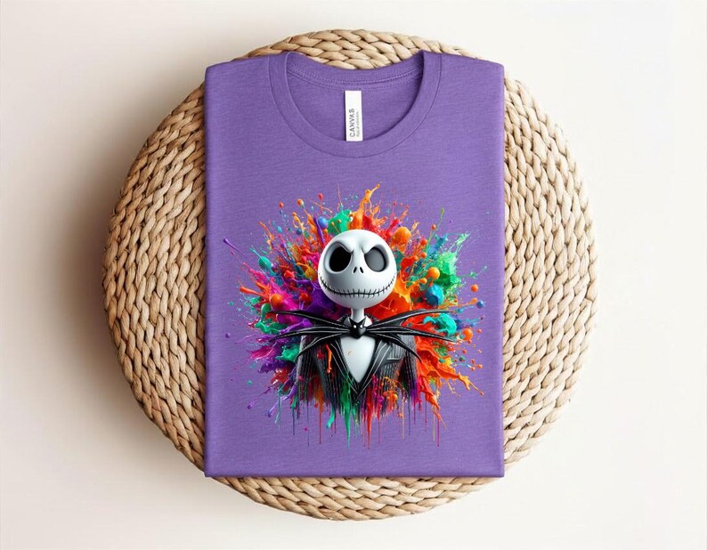 May include: A purple t-shirt featuring a graphic of a white skull character with a stitched mouth wearing a black pinstripe suit and bow tie, centered against a vibrant, multi-colored paint splatter design with splashes of red, blue, green, and orange.