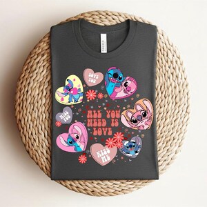 Peut inclure: T-shirt gris fonc&eacute; avec des personnages de dessins anim&eacute;s dans des c&oelig;urs. Les c&oelig;urs sont roses, jaunes et blancs, avec les textes "Love You" et "Kiss Me". Le t-shirt porte &eacute;galement l'inscription "All You Need Is Love" en rouge.