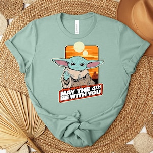 Może przedstawiać: Jasnozielona koszulka z nadrukiem zielonego kosmity z dużymi uszami na pomarańczowo-ż&oacute;łtym tle. Pod postacią widnieje napis "STAR WARS DAY MAY THE 4TH BE WITH YOU". Koszulka jest zawiązana na dole.