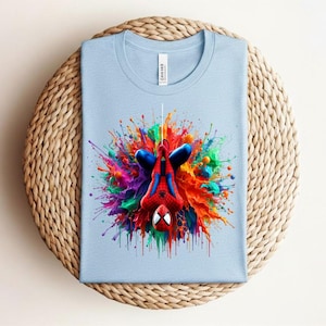 May include: A light blue t-shirt featuring a colorful graphic of Spider-Man hanging upside down. The superhero is depicted in his classic red and blue suit, surrounded by a vibrant explosion of paint in various colors. The shirt is made of a soft material.