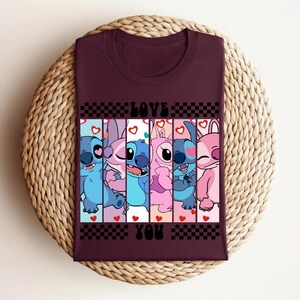 May include: Burgundy t-shirt featuring a colorful graphic of cartoon characters with the words "LOVE YOU" in a checkerboard design. The characters are in shades of blue and pink, with hearts.