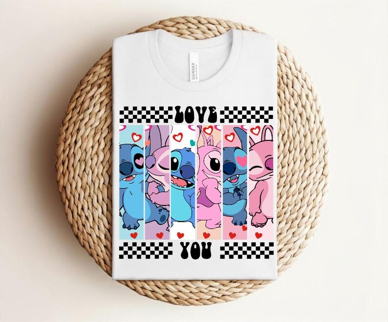May include: White t-shirt featuring a colorful graphic of cartoon characters with the words "LOVE YOU" in black. The design includes blue, pink, and purple characters with hearts and a checkered pattern.