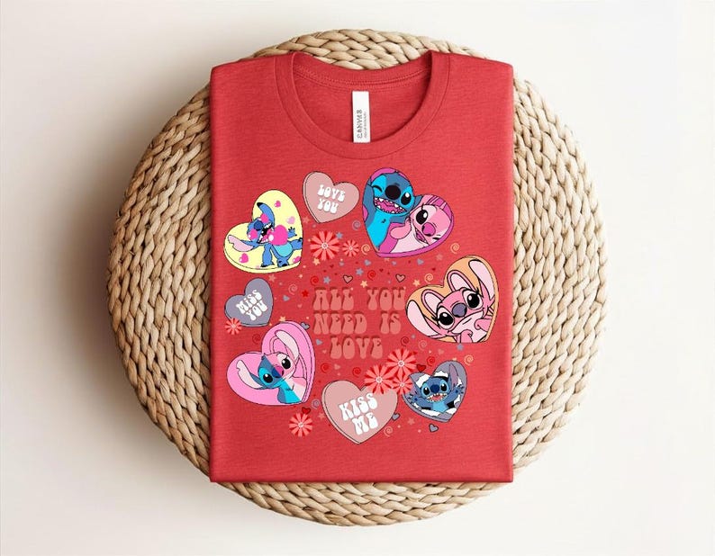Peut inclure: T-shirt rouge avec des personnages de dessins anim&eacute;s en forme de c&oelig;ur, avec les phrases "Love You" et "Kiss Me". Le t-shirt porte &eacute;galement l'inscription "All You Need Is Love". Le t-shirt est pr&eacute;sent&eacute; sur une surface tiss&eacute;e.