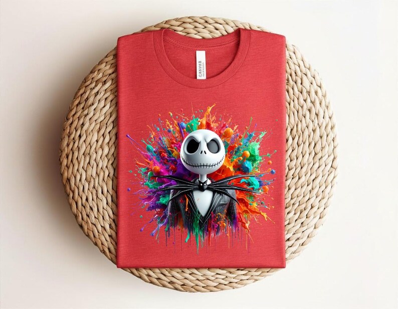 May include: A red crew neck t-shirt featuring a graphic of a white skeletal character with a black pinstripe suit and bow tie, centered against a vibrant, multi-colored paint splatter background with hues of blue, green, yellow, and pink.