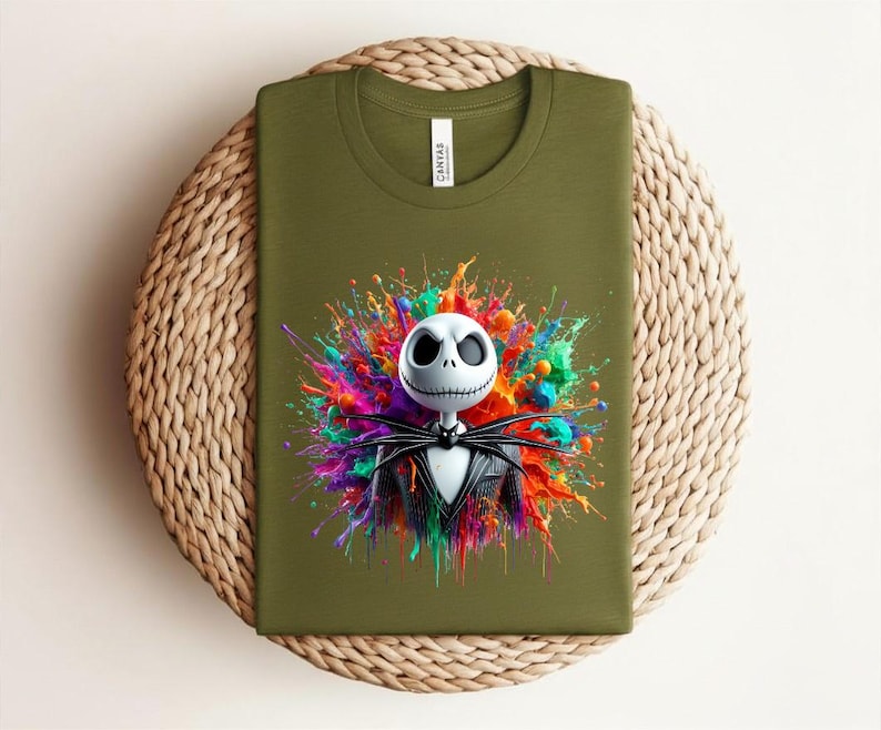 May include: An olive green t-shirt featuring a graphic of a white skull character with large black eyes and a stitched mouth, wearing a black pinstripe suit and bow tie, set against a vibrant, multi-colored paint splatter background.