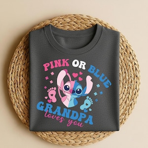 Pu&ograve; includere: T-shirt grigio scuro con un personaggio dei cartoni animati diviso in rosa e blu, con la scritta "PINK OR BLUE" sopra e "GRANDPA loves you" sotto. Il design include cuori, impronte e dettagli floreali.