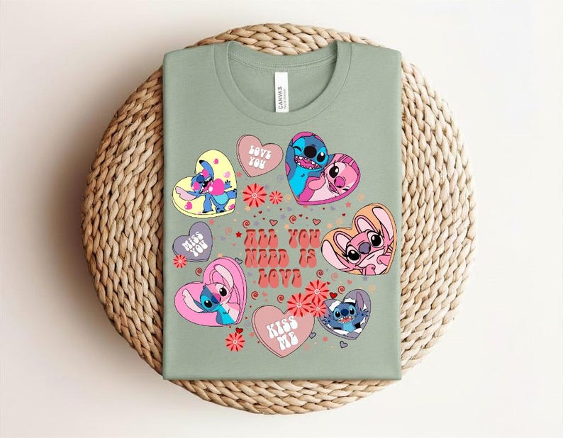 Peut inclure: T-shirt vert sauge avec des personnages de dessins anim&eacute;s dans des motifs en forme de c&oelig;ur. Les c&oelig;urs portent des phrases comme "Love You" et "Kiss Me". Le texte "All You Need Is Love" est &eacute;galement pr&eacute;sent. Le t-shirt est pr&eacute;sent&eacute; sur un tapis rond tiss&eacute;.