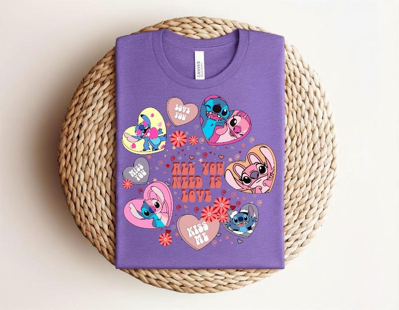 Peut inclure: Un t-shirt violet avec un motif color&eacute; de personnages de dessins anim&eacute;s en forme de c&oelig;ur. Le t-shirt porte l'inscription "All You Need Is Love" et d'autres phrases comme "Love You" et "Kiss Me".