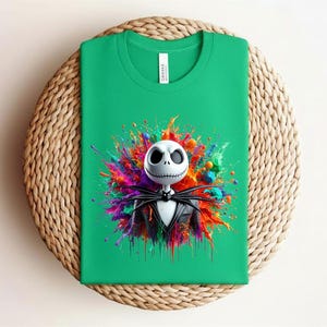 May include: A bright green t-shirt featuring a graphic of a white skull character with large black eyes and a stitched mouth, wearing a black pinstripe suit and bat bowtie, centered against a vibrant, multi-colored paint splatter background.