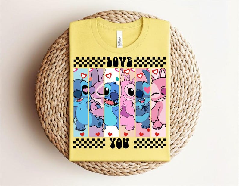 May include: Yellow t-shirt featuring a graphic of cartoon characters in blue, pink, and purple, with the words "LOVE YOU" in black. The design includes hearts and a checkered pattern.