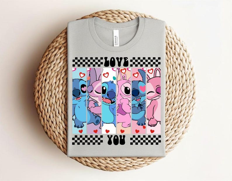 May include: A light gray t-shirt featuring a colorful graphic of cartoon characters. The design includes the words "LOVE YOU" in a checkered pattern. The characters are in shades of blue, pink, and purple, with hearts.