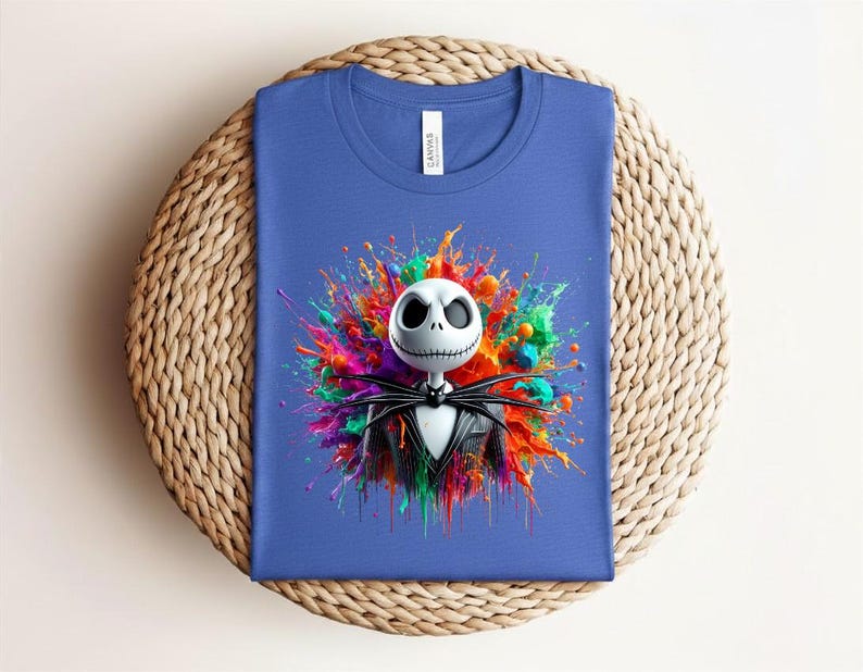 May include: A blue t-shirt featuring a graphic of a white skeletal character with a black pinstripe suit and bow tie, centered against a vibrant, multi-colored paint splatter background. The shirt has a white neck label with the text CANVAS.