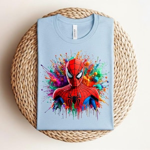 Op de afbeelding: Lichtblauw T-shirt met een Spider-Man afbeelding. De superheld is afgebeeld in zijn rood-zwarte pak, omringd door kleurrijke verfspatten. Het T-shirt is gemaakt van een zachte stof.