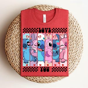 May include: Red t-shirt featuring a graphic of cartoon characters in shades of blue and pink, with the words "LOVE YOU" in black. The design includes hearts and a checkered pattern.