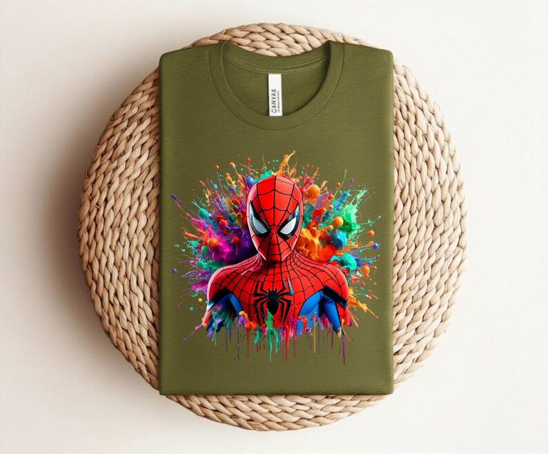 Op de afbeelding: Olijfgroen t-shirt met een kleurrijke Spider-Man-afbeelding. De superheld is afgebeeld in zijn rood-blauwe pak, met een zwart spinnenembleem op zijn borst. De achtergrond heeft levendige verfspatten.