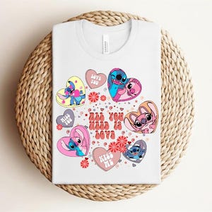 Peut inclure: T-shirt blanc avec un motif color&eacute; de personnages de dessins anim&eacute;s en forme de c&oelig;ur. Le motif comprend le texte "All You Need Is Love", ainsi que des phrases comme "Love You" et "Kiss Me".