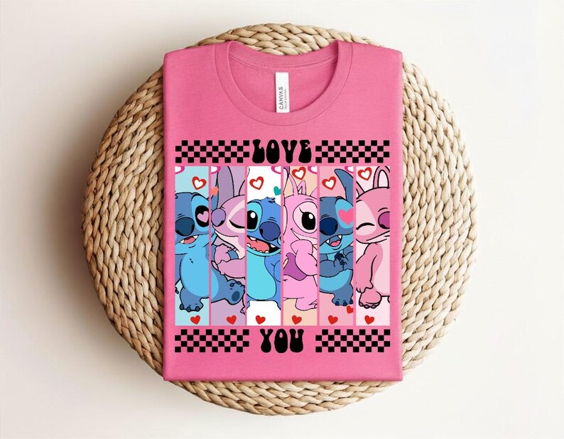 May include: A pink t-shirt featuring a graphic of several cartoon characters with the words "LOVE YOU" in black. The characters are in various shades of blue and pink, with hearts and checkered patterns.