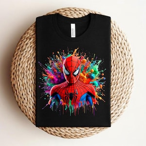 Op de afbeelding: Zwart t-shirt met een kleurrijke afbeelding van Spider-Man. De superheld is afgebeeld in zijn klassieke rood-blauwe pak, met een levendige splash van kleuren erachter. Het shirt is op een geweven oppervlak gevouwen.