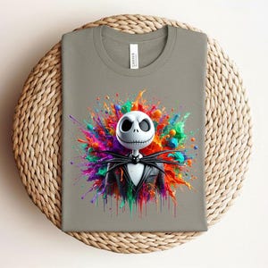 May include: A grey t-shirt featuring a graphic of a white skull character with a black pinstripe suit and bow tie, centered against a vibrant, multi-colored paint splatter design with hues of pink, blue, orange, green, and yellow.
