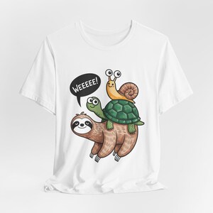 Peut inclure: T-shirt blanc avec un dessin animé d'un paresseux, d'une tortue et d'un escargot. Le paresseux est marron, la tortue est verte et l'escargot est jaune. L'escargot est sur la tortue, et la tortue est sur le paresseux. Une bulle de dialogue dit "WEEEEEE!"